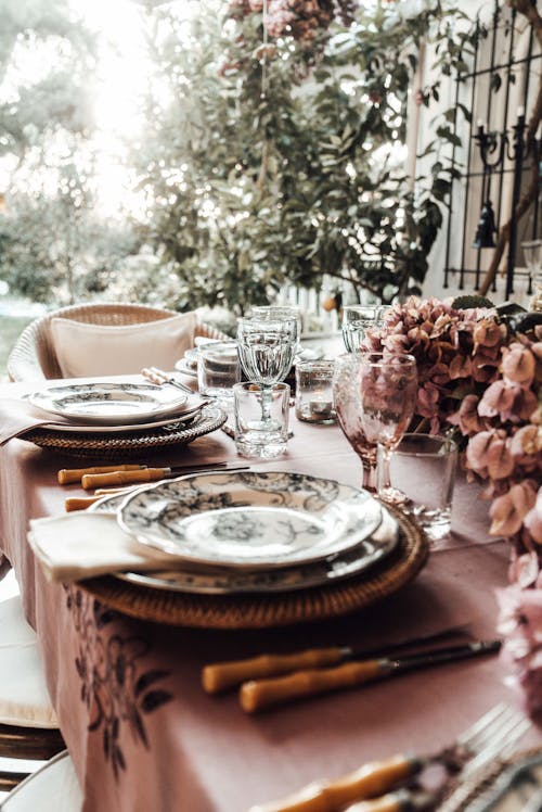 Banquet table with dishware and wineglasses near bunches of flowers