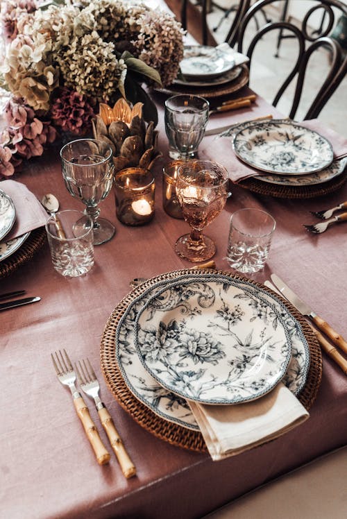 High angle of plates with cutlery placed near glassware on table decorated with burning candle and blooming flowers