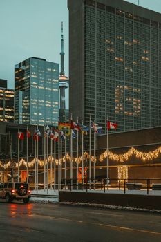 Urban scene of Toronto featuring the CN Tower and flags at dusk with festive lights.