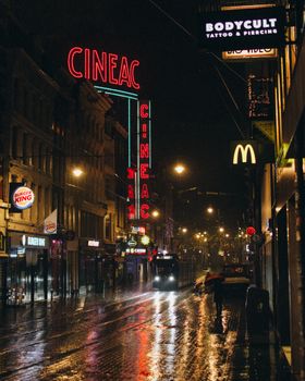 Capture the vibrant nightlife of Amsterdam with neon signs reflecting on wet streets during a rainy night.