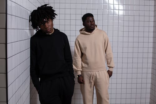 Confident African American males in comfy clothes standing with hands in pockets in tiles room