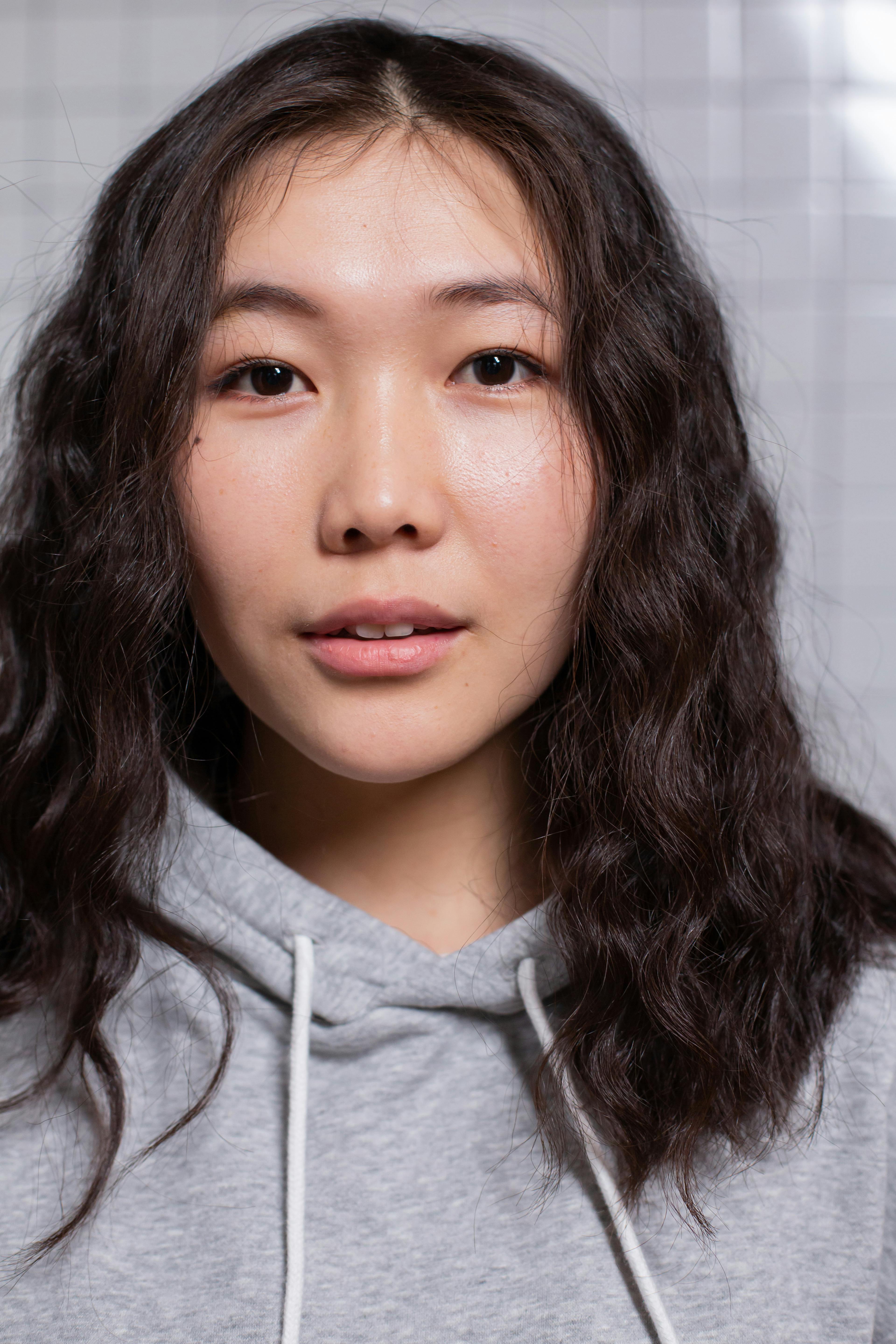 Self assured young Asian lady with dark wavy hair and perfect skin looking at camera against gray background