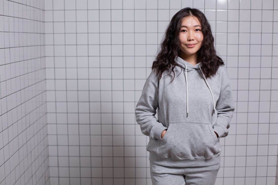 Young pleasant Asian woman in hoodie near tiled wall