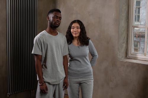 Confident young African American man near smiling content ethnic woman looking at camera near concrete wall of modern flat