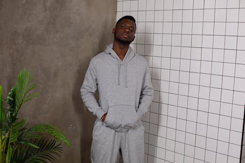 Confident young African American male with hands in pockets looking at camera near potted verdant plant and tiled wall