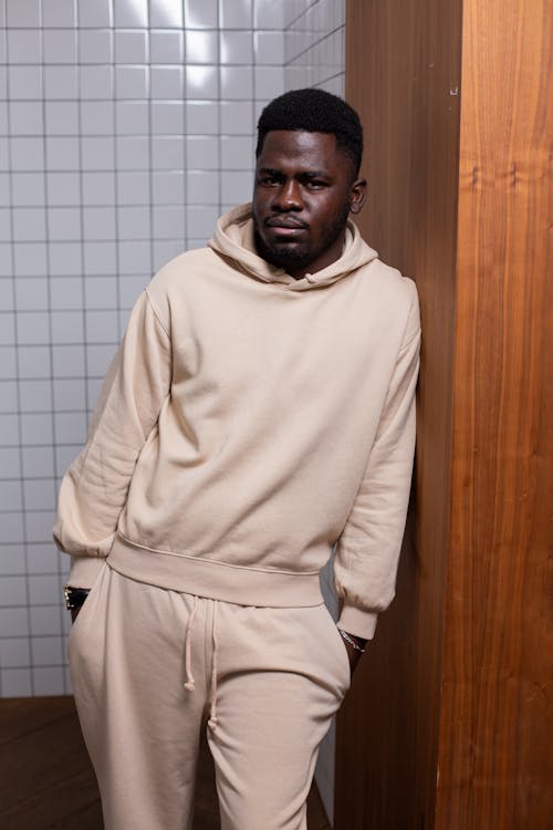 Black man with hands in pocket leaning on wooden wall