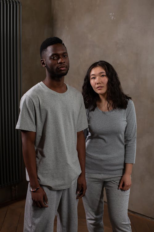 Young Asian woman and black man in gray sportswear looking at camera in modern studio