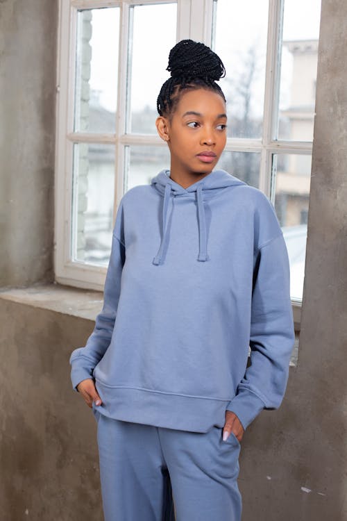 Thoughtful young African American female in blue stylish hoodie and trousers looking away near window