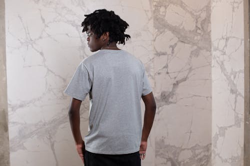 Back view of pensive young African American man with dreadlocks near wall with abstract patterns