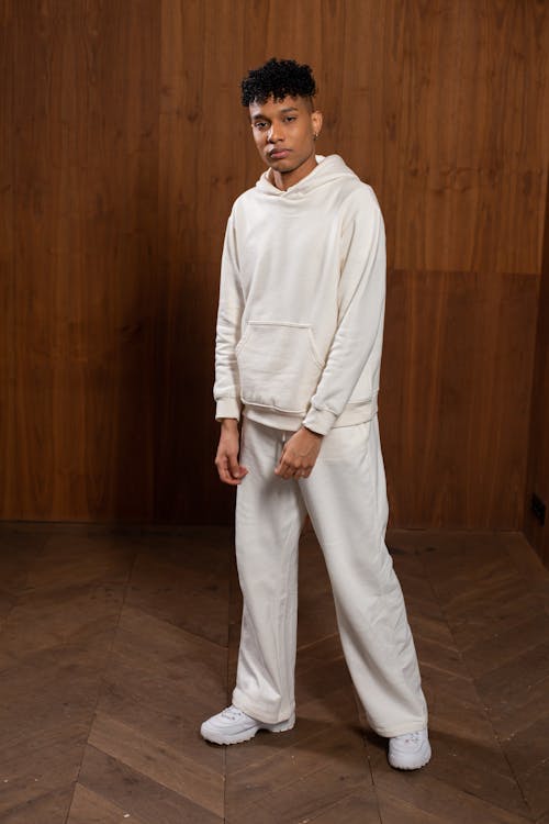 Full body of young African American male in stylish white trousers and hoodie looking at camera