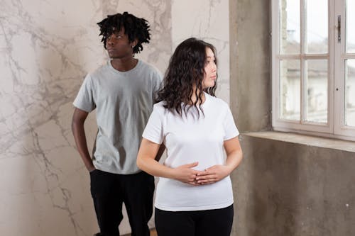 Young carefree multiracial man and woman looking away among gray walls near window in daytime
