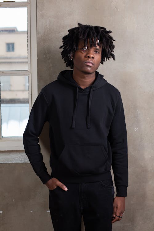 Free Young African American male with dreadlocks in trendy black activewear looking at camera near gray wall Stock Photo