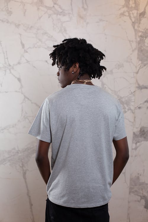 Back view of young African American male with trendy dreadlocks looking over shoulder near wall with abstract patterns