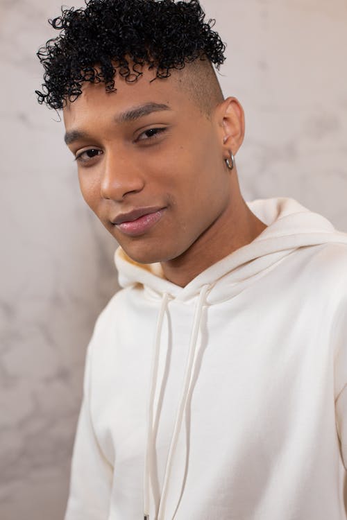Crop African American male with earring wearing white hoodie gently smiling at camera