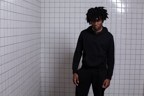 Fashionable young man with dreadlocks in a modern tiled room wearing a black hoodie.