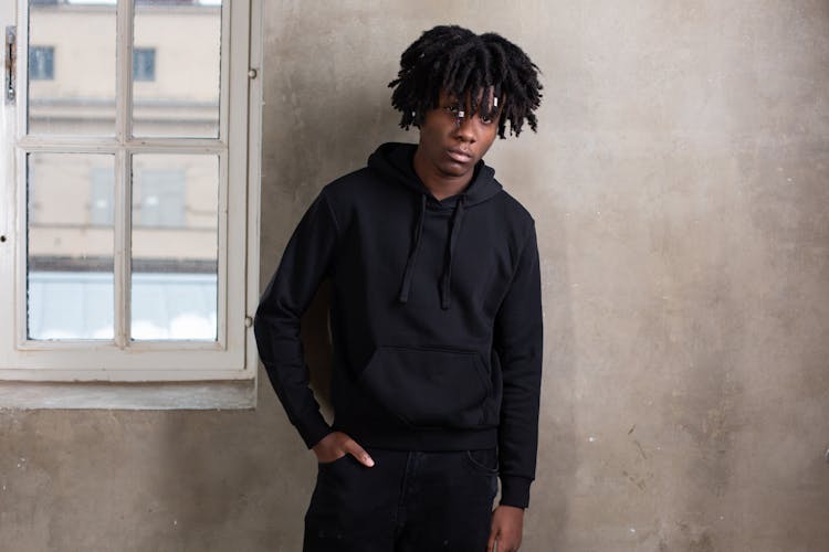 Serious Black Guy In Hoodie Standing Near Gray Wall