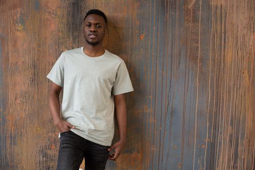 Free Positive young bearded African American guy in white t shirt standing near wooden wall with hand in pocket and looking at camera Stock Photo