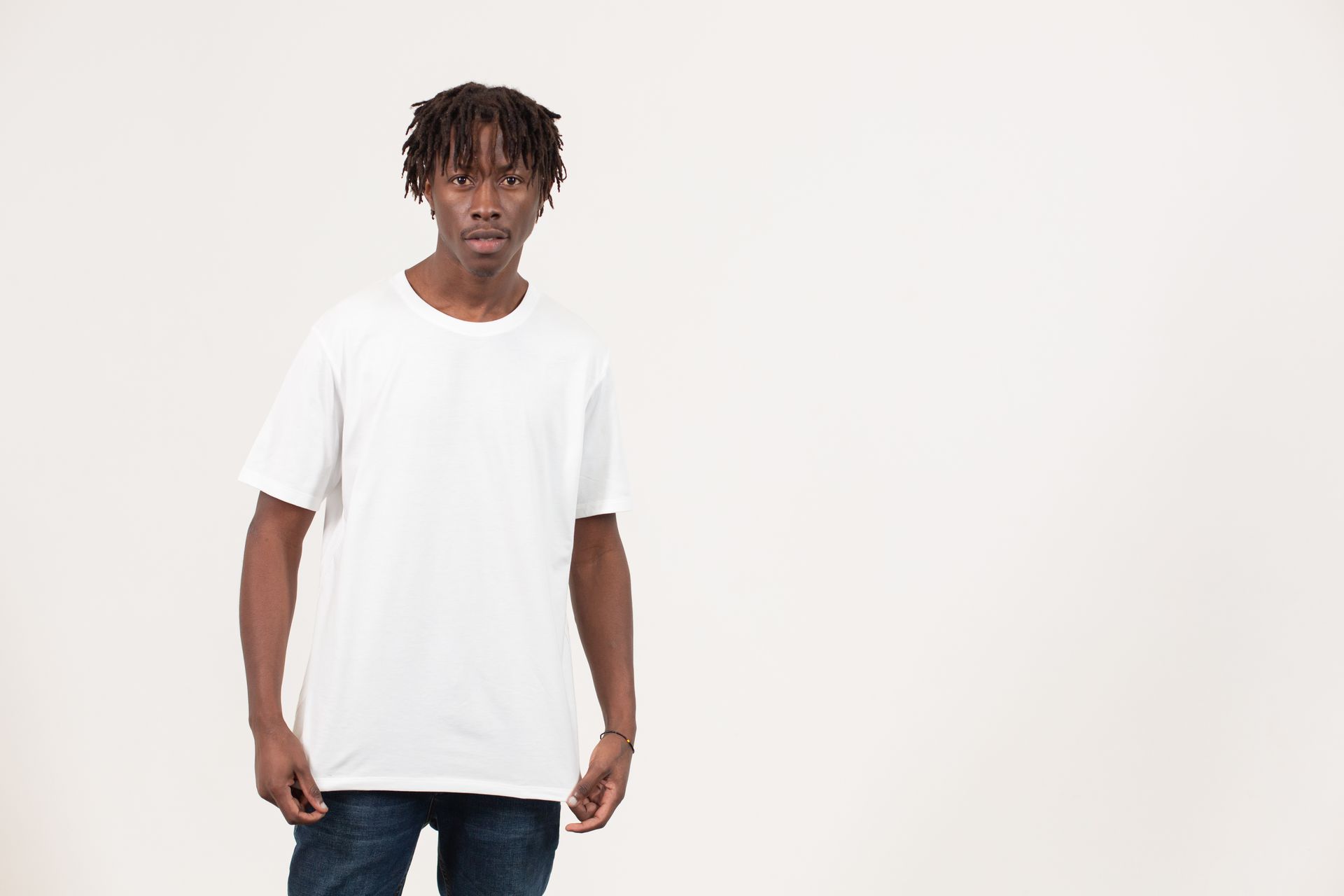 Serious young African American male model in simple white t shirt and jeans standing in light studio and looking at camera
