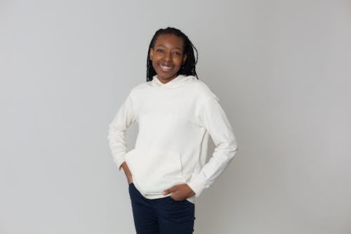 Cheerful black woman in casual wear standing in light studio