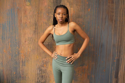 Confident black sportswoman in activewear standing near wooden wall
