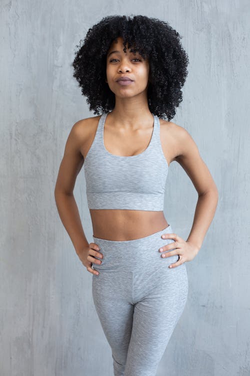 Fit black sportswoman in gray activewear standing in light studio