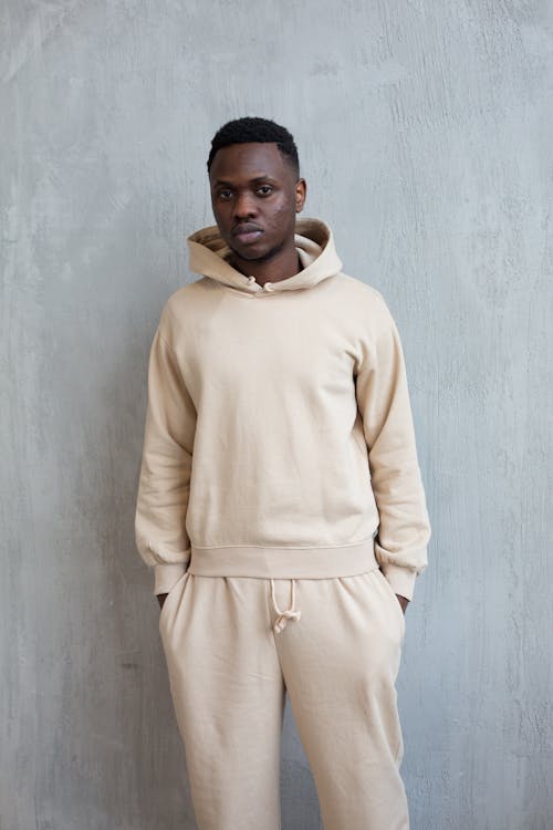Confident young African American guy in white hoodie and pants standing in light studio on white background and looking at camera