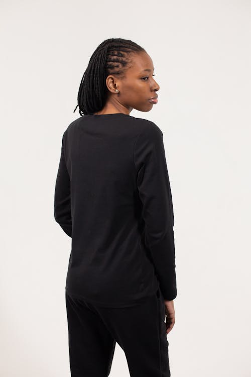 Back view of African American lady wearing black blouse and pants while standing in bright studio on white background and looking over shoulder