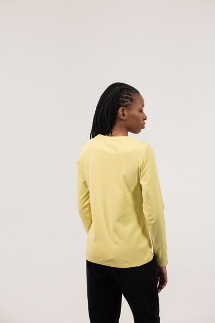 Back view of African American female wearing yellow blouse and black pants while standing in bright studio on white background and looking away