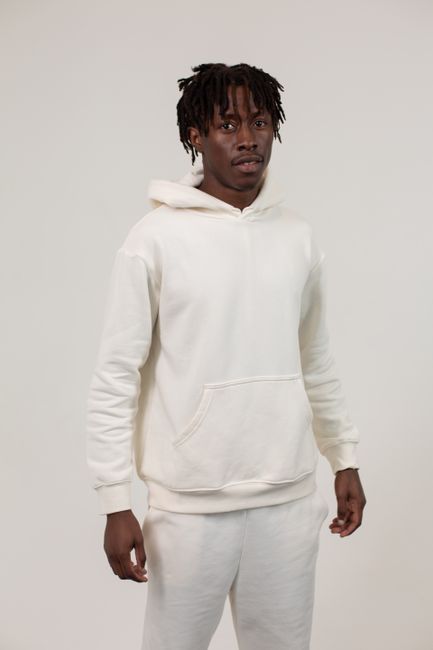 Serious young black male in white hoodie and pants standing on white background in bright studio and looking at camera