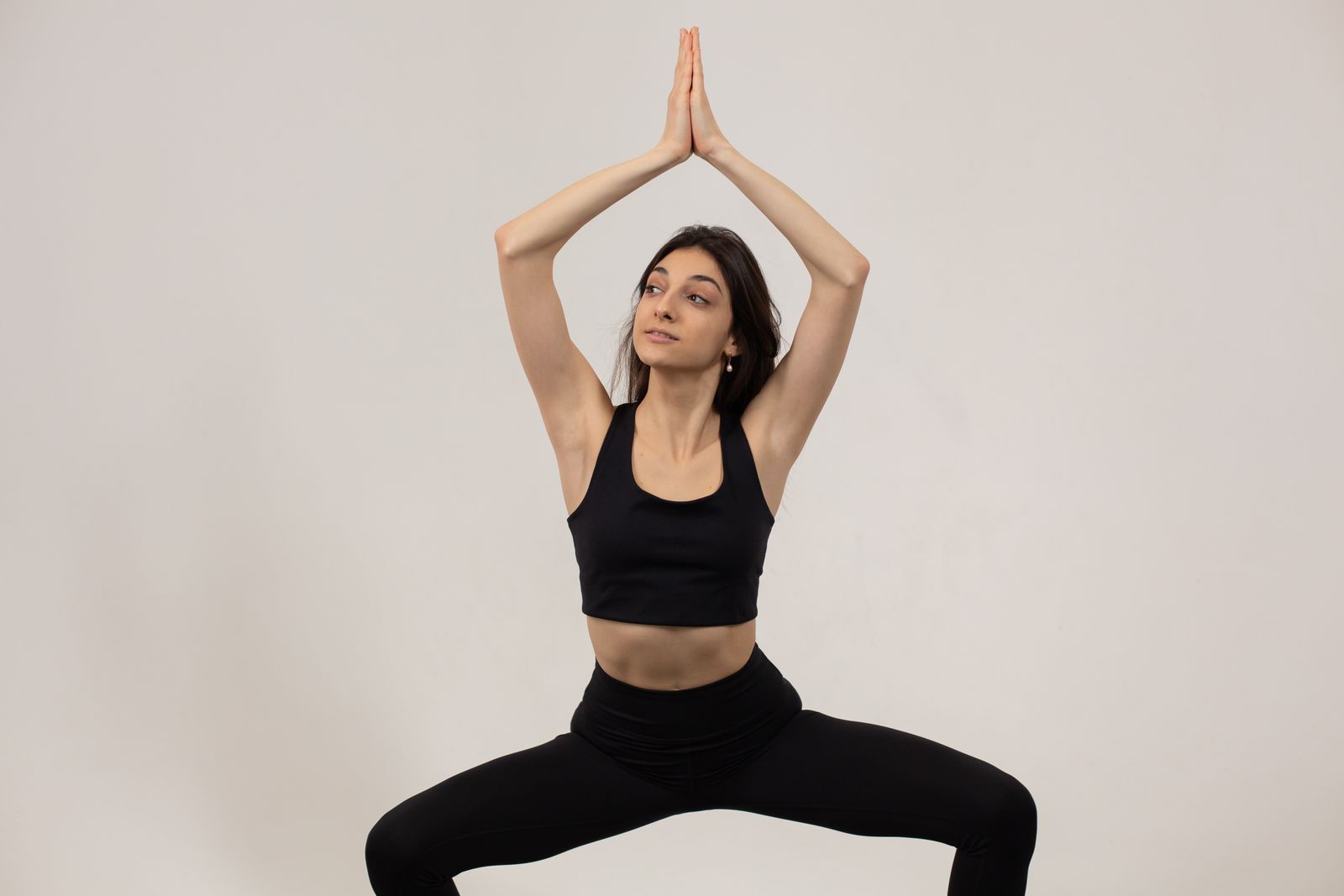 Woman demonstrating utkatasana chair pose with arms raised overhead in namaste position