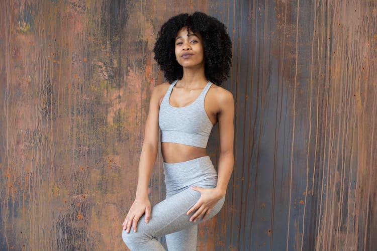 Confident Black Woman In Activewear Standing Against Wooden Wall