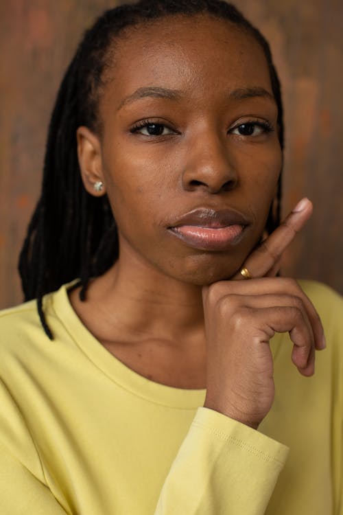 Portrait of independent African American female with dreads wearing yellow blouse and touching face while looking at camera