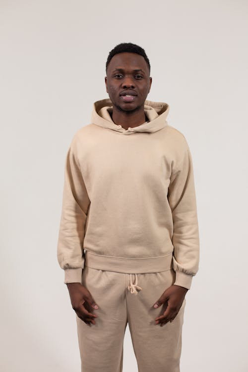 Confident African American male model wearing stylish beige sportive clothes and looking at camera while standing against beige background