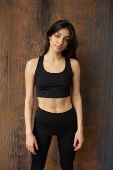 Slim young lady dressed in activewear standing in front of wooden wall and looking at camera