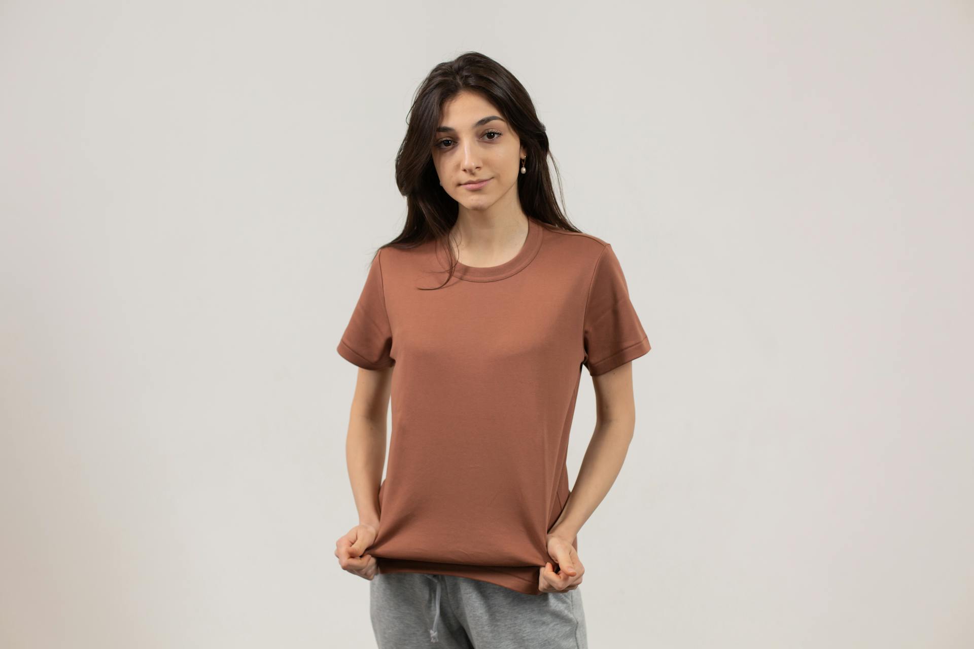 Trendy young woman poses confidently in a brown t-shirt and grey trousers, embodying contemporary casual style.