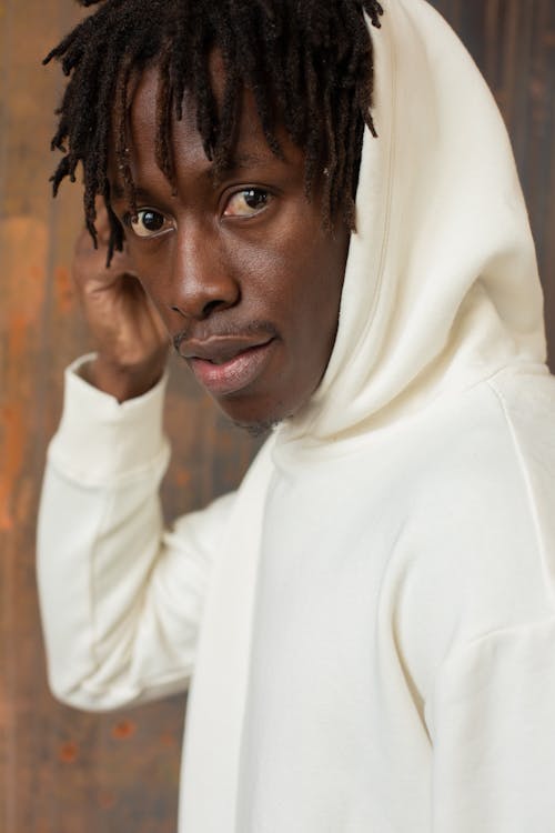 Side view of African American male with dreadlocks adjusting hood of trendy sweatshirt and looking at camera