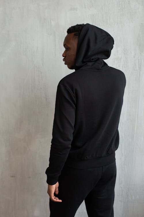Free Back view of African American male in sports suit with hood on head standing against gray background Stock Photo