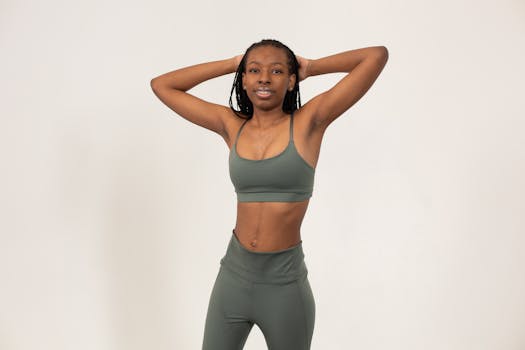 Positive slim African American female with hands on head wearing sports bra and leggings smiling and looking at camera