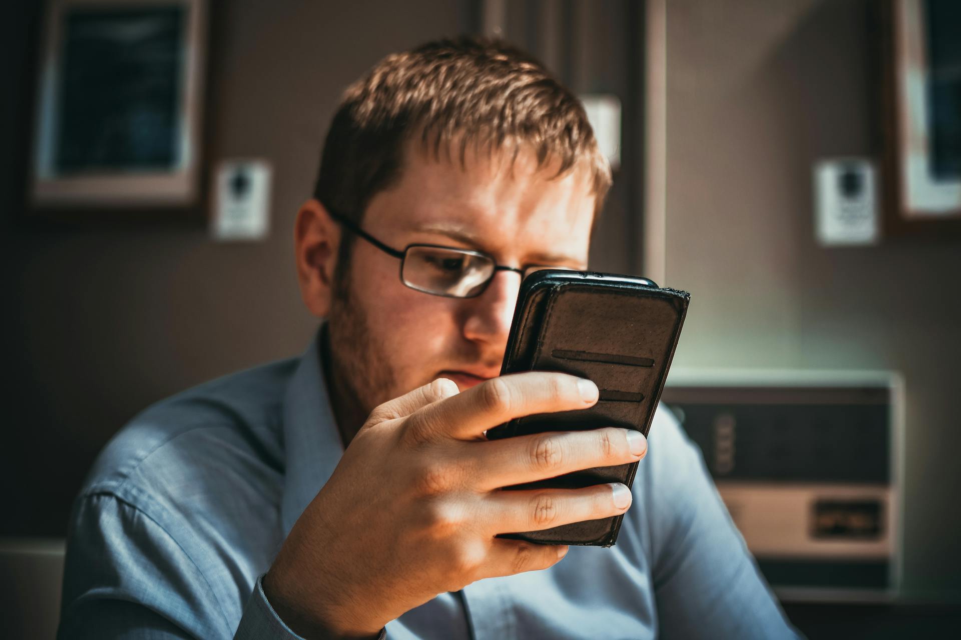 Serious businessman wearing glasses focused on smartphone in a modern office setting.