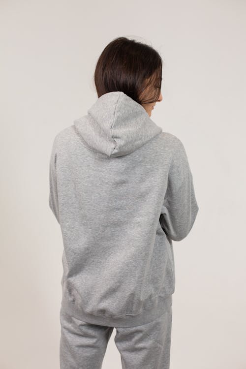 Back view of young female wearing oversize hoodie and sweatpants standing against white background