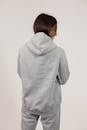 Back view of young female wearing oversize hoodie and sweatpants standing against white background