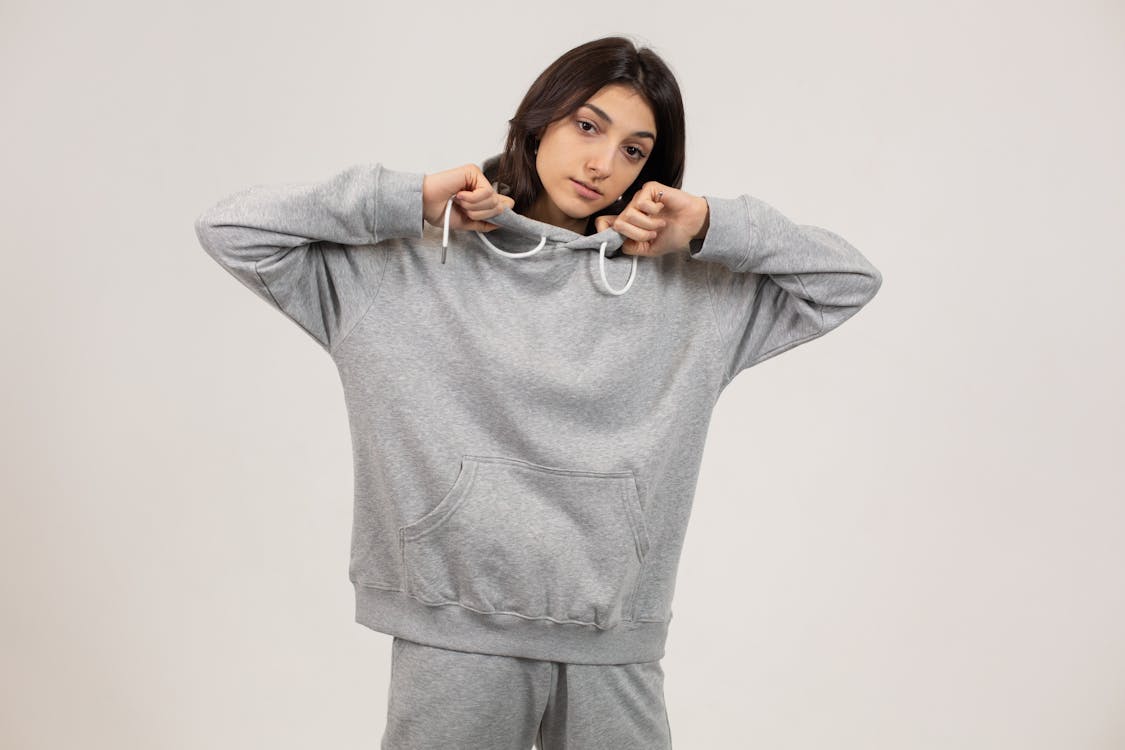 Free Serious female wearing oversize hoodie and sweatpants standing against white background and looking at camera Stock Photo