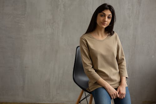 Wanita Dengan Kemeja Lengan Panjang Coklat Dan Jeans Denim Biru Duduk Di Kursi Hitam