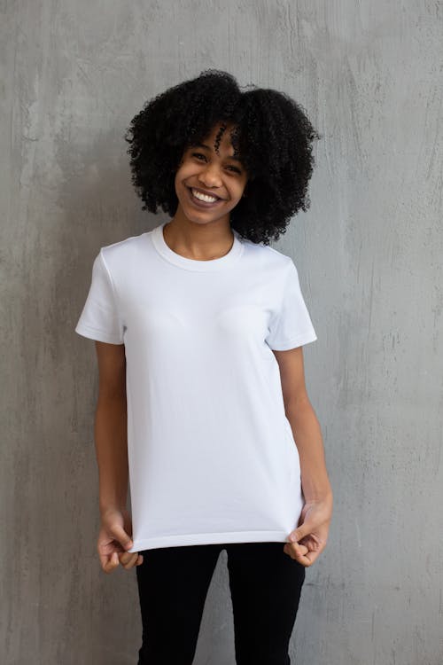 Free Charming African American female in white t shirt and tight pants smiling widely and looking at camera Stock Photo