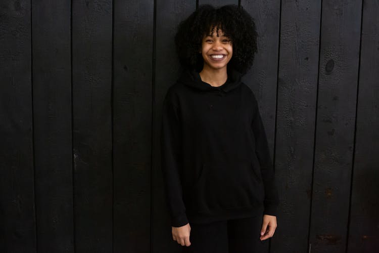 Smiling Black Woman In Hoodie Against Wooden Wall