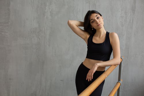 Free Fit female athlete in sportswear leaning on barre standing with hand on head and looking at camera Stock Photo