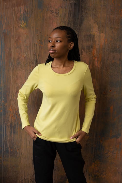 African American female in long sleeve t shirt and pants standing with hands in pockets and looking away