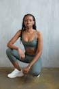 Full body of confident African American female athlete in activewear squatting on floor near gray wall and looking at camera
