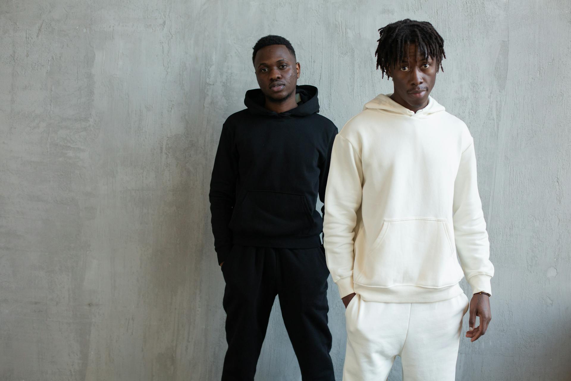 Black men in trendy outfit standing against cement wall