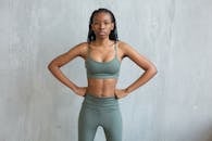 Confident young African American female in crop top and leggings standing near gray wall with hands on hips and looking at camera